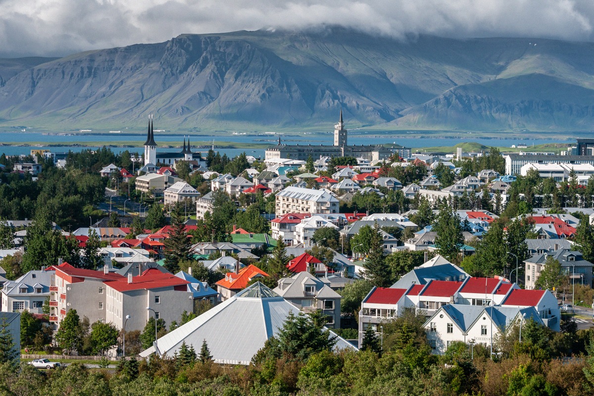 Stadtpanorama von Reykjavík mit bunten Hausdächern, Kirchturm und den Bergen im Hintergrund